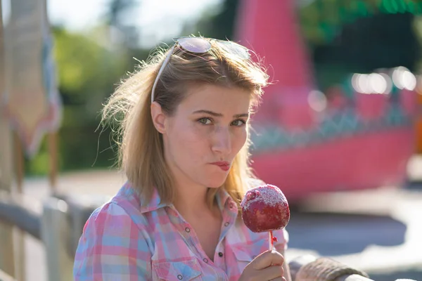 pretty young woman eating and biting red caramel apple in the park in the sunny day
