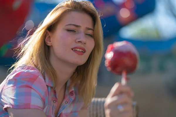 stock image pretty young woman eating and biting red caramel apple in the park in the sunny day