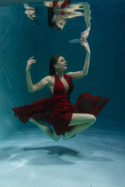 красивая свободная дайвер женщина плавает в длинном красном вечернем платье под водой в одиночку в глубокой
