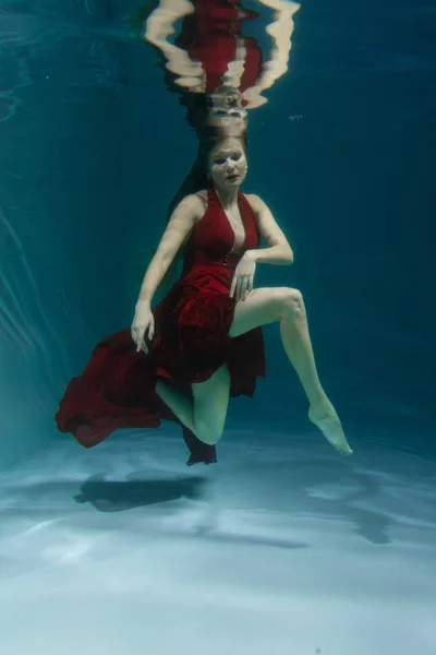 深いだけで水の下の長い赤いイブニング ドレスで泳いでいる美しい無料ダイバー女性 — ストック写真