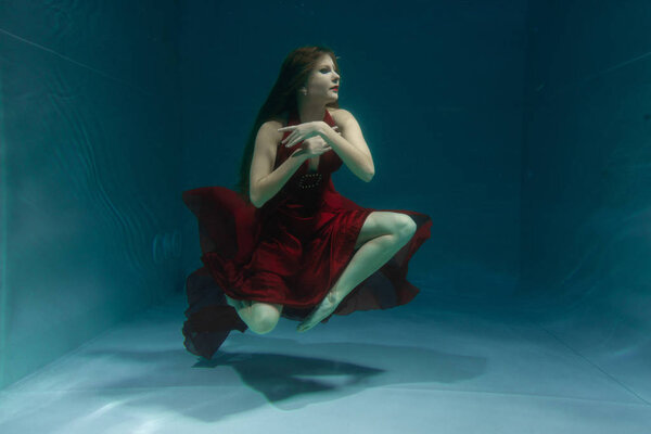 beautiful free diver woman swimming in long red evening dress under water alone in the deep