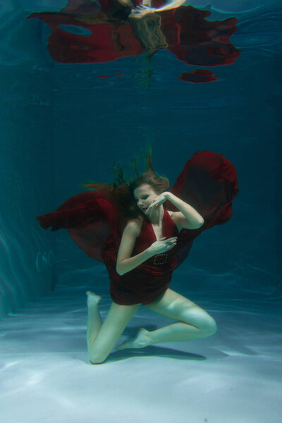 красивая свободная дайвер женщина плавает в длинном красном вечернем платье под водой в одиночку в глубокой

