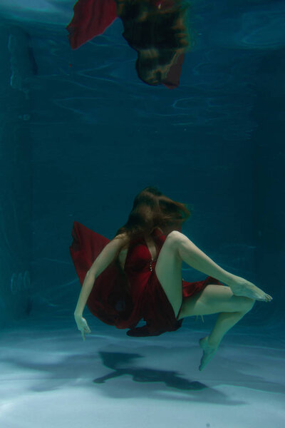 красивая свободная дайвер женщина плавает в длинном красном вечернем платье под водой в одиночку в глубокой
