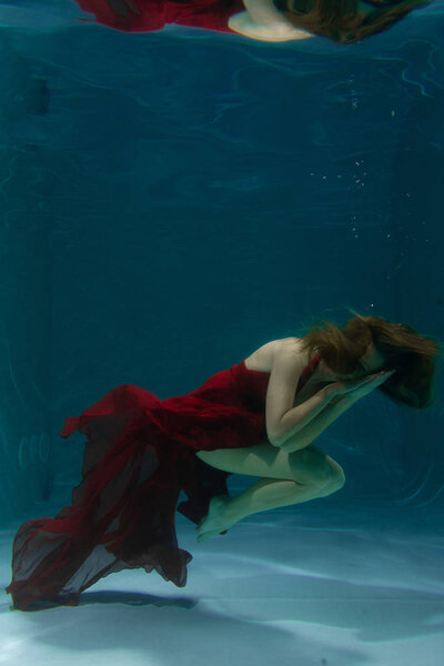 beautiful free diver woman swimming in long red evening dress under water alone in the deep