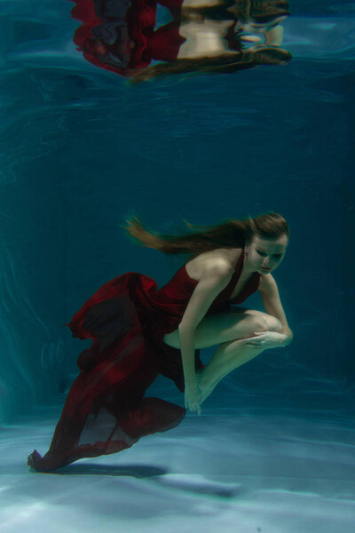 красивая свободная дайвер женщина плавает в длинном красном вечернем платье под водой в одиночку в глубокой
