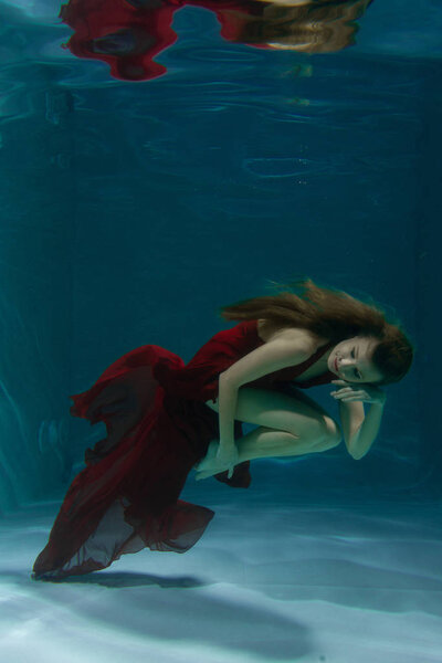 красивая свободная дайвер женщина плавает в длинном красном вечернем платье под водой в одиночку в глубокой
