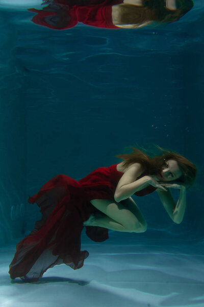 красивая свободная дайвер женщина плавает в длинном красном вечернем платье под водой в одиночку в глубокой
