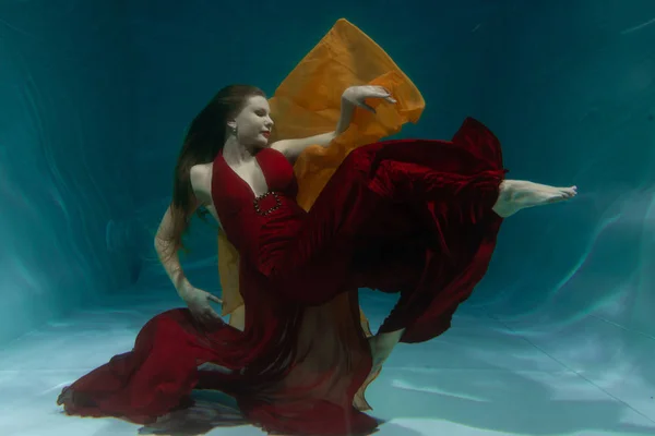 beautiful free diver woman swimming in long red evening dress under water alone in the deep