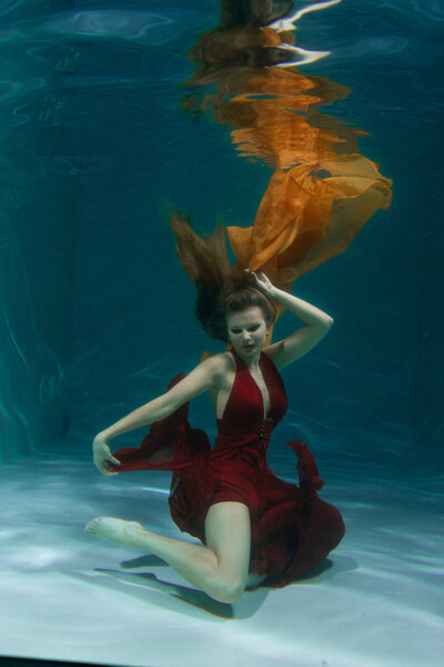 красивая свободная дайвер женщина плавает в длинном красном вечернем платье под водой в одиночку в глубокой
