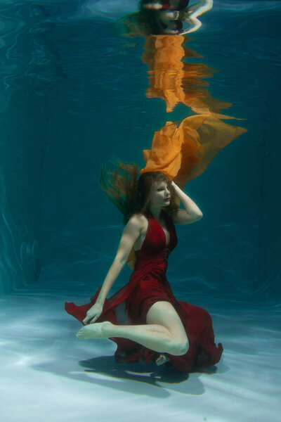 красивая свободная дайвер женщина плавает в длинном красном вечернем платье под водой в одиночку в глубокой
