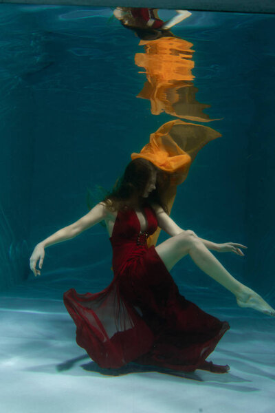 красивая свободная дайвер женщина плавает в длинном красном вечернем платье под водой в одиночку в глубокой
