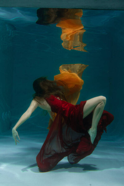 красивая свободная дайвер женщина плавает в длинном красном вечернем платье под водой в одиночку в глубокой
