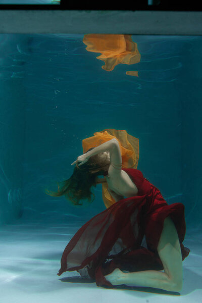 красивая свободная дайвер женщина плавает в длинном красном вечернем платье под водой в одиночку в глубокой
