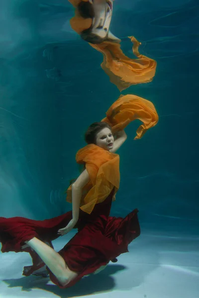 深いだけで水の下の長い赤いイブニング ドレスで泳いでいる美しい無料ダイバー女性 — ストック写真
