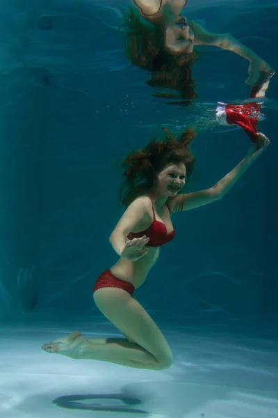 funny happy girl in swimming pool wearing red santa lingerie with holiday hat and swimming underwater in the deep alone