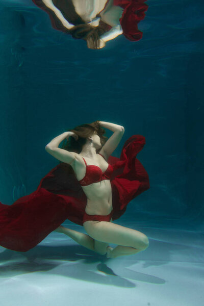 довольно кавказские длинные волосы женщина плавает под водой в красном сексуальном белье в одиночестве в глубине
