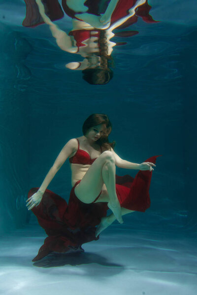 довольно кавказские длинные волосы женщина плавает под водой в красном сексуальном белье в одиночестве в глубине
