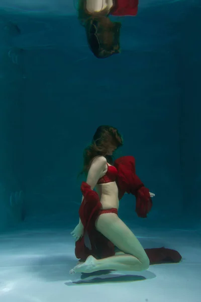 漂亮的白种人长发女人游泳在水下的红色性感内衣单独在深 — 图库照片