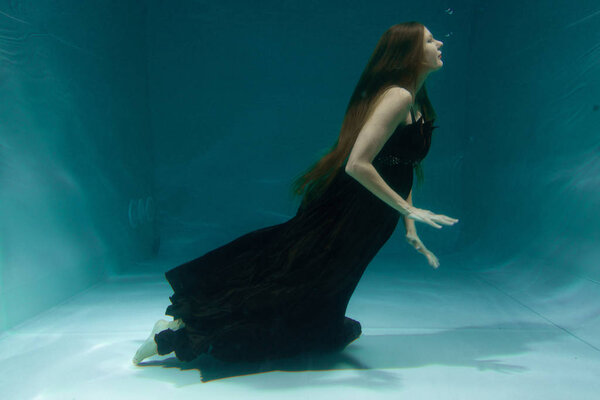 beautiful lady in long evening dress swimming underwater on the deep alone