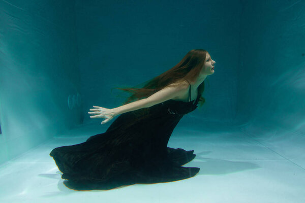 beautiful lady in long evening dress swimming underwater on the deep alone