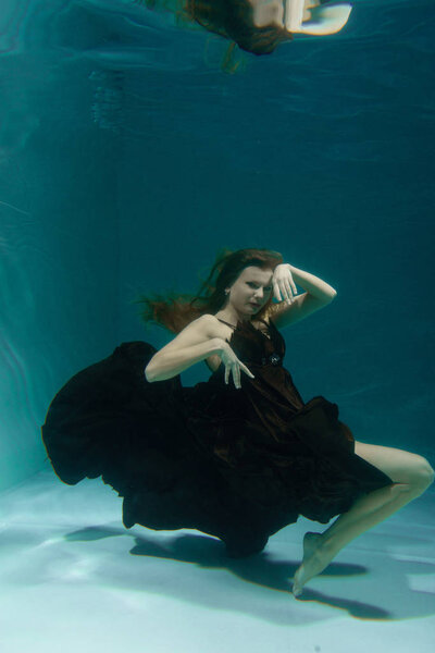 beautiful lady in long evening dress swimming underwater on the deep alone