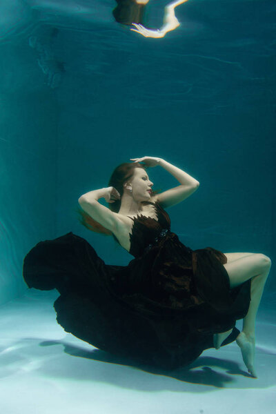 beautiful lady in long evening dress swimming underwater on the deep alone