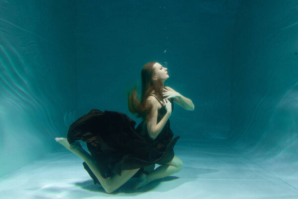 beautiful lady in long evening dress swimming underwater on the deep alone