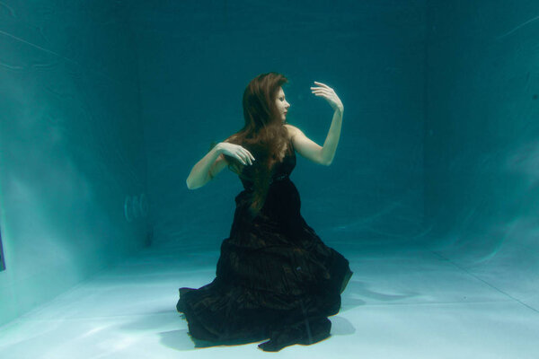 beautiful lady in long evening dress swimming underwater on the deep alone