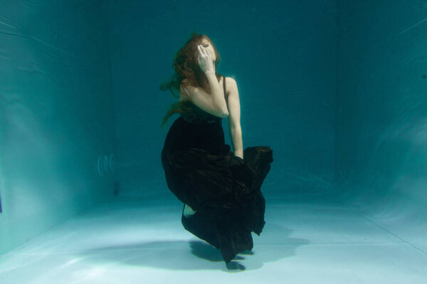 beautiful lady in long evening dress swimming underwater on the deep alone