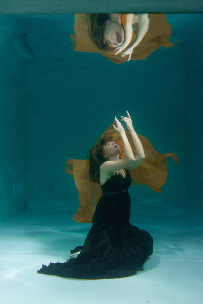 красивая леди в длинном вечернем платье плавает под водой в одиночестве
