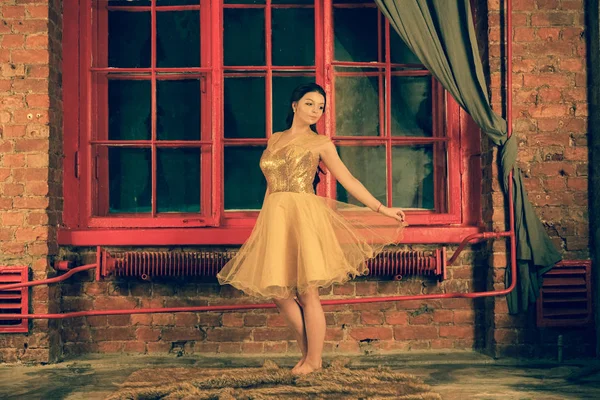 美丽的高加索女孩在金色的亮片礼服在一个巨大的夜晚红色窗口与灰色窗帘的背景 — 图库照片