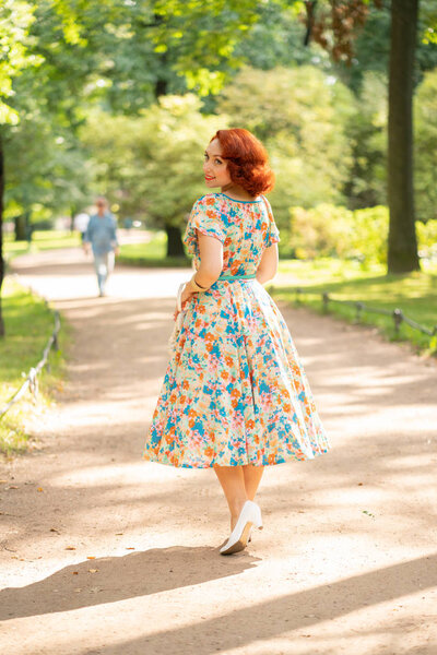 cute caucasian girl with red bob haircut in retro dress enjoying life in city Park in summer sunny day