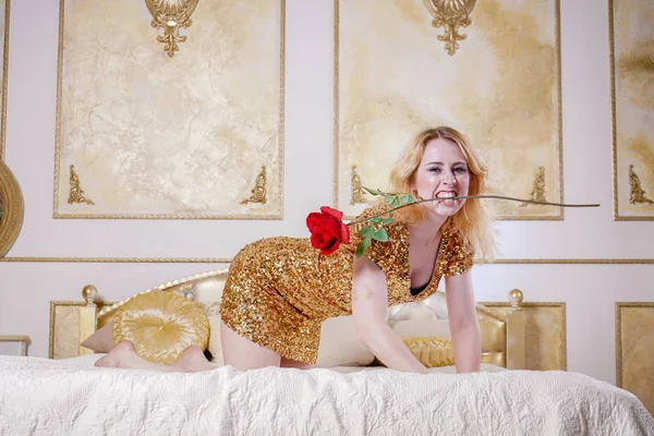 cute girl in gold sequin dress resting on a white bed in a room with stucco on the walls