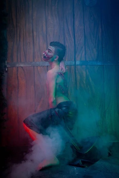 scary vampire male with huge teeth and bloody body as halloween body art standing in the night smoke alone