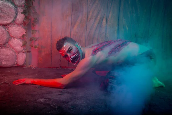 scary vampire male with huge teeth and bloody body as halloween body art standing in the night smoke alone