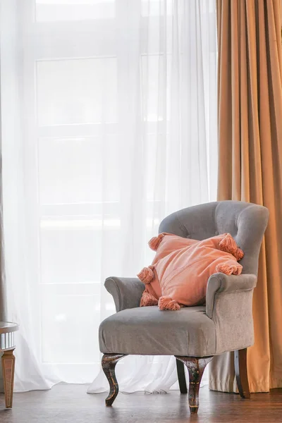 pink pillows with tassels on the cozy grey chair near the window. nobody.