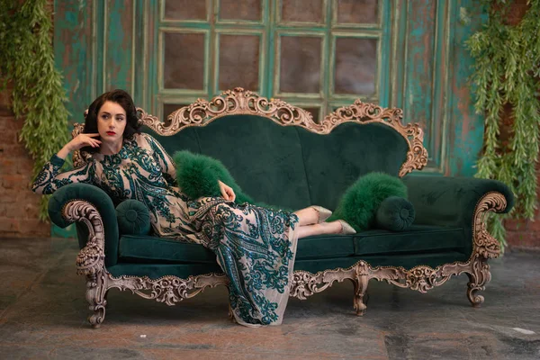 优雅的高加索女孩在一个豪华的长亮片蕾丝礼服与绿色蓬松的 Boa 在她的手中摆姿势在复古房间与复古豪华家具 — 图库照片