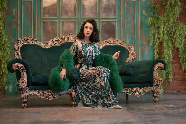 优雅的高加索女孩在一个豪华的长亮片蕾丝礼服与绿色蓬松的 Boa 在她的手中摆姿势在复古房间与复古豪华家具 — 图库照片