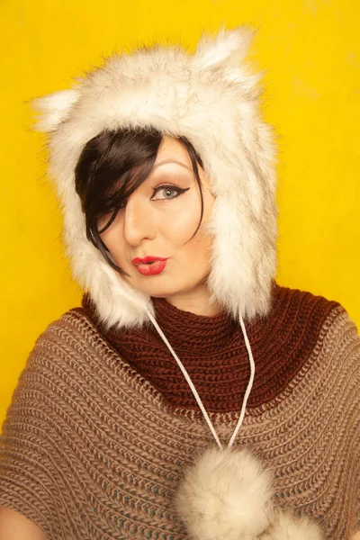 charming caucasian girl in a fur white hat with cat ears smiles and enjoys life on a yellow solid background in the Studio alone