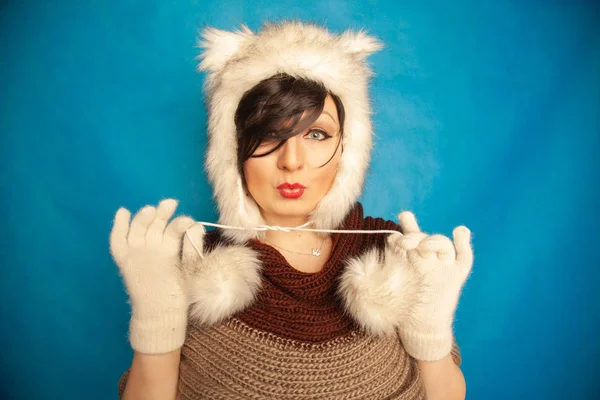 charming caucasian girl in a fur white winter hat with cat ears smiles and enjoys life on a blue solid background in the Studio alone