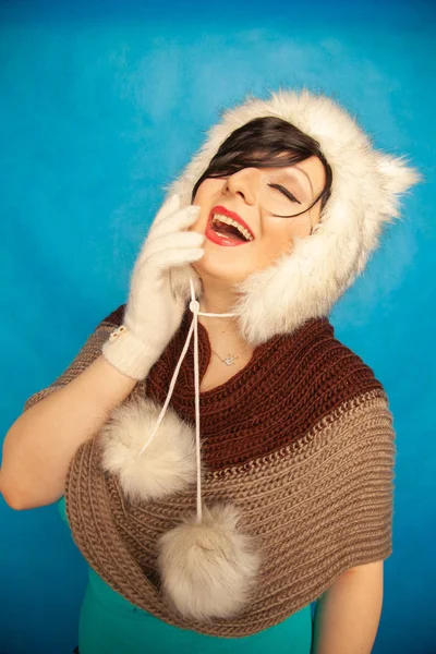 charming caucasian girl in a fur white winter hat with cat ears smiles and enjoys life on a blue solid background in the Studio alone