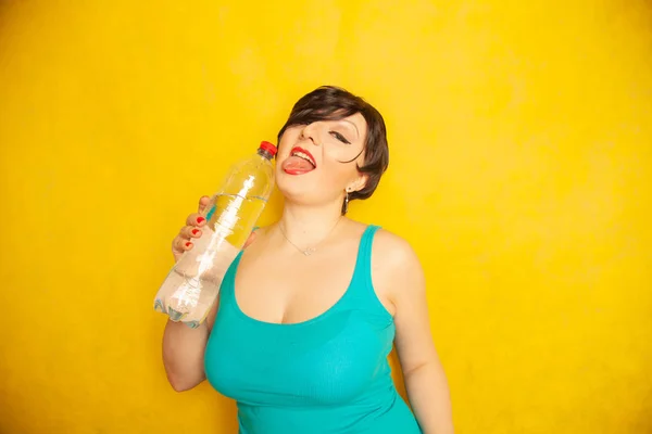 スタジオで背景が黄色の水の大きなボトルと短い髪で陽気な女の子 — ストック写真