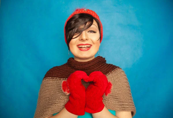 pretty brunette girl wearing fashion red knitted winter gat and warm beautiful gloves on blue studio solid background