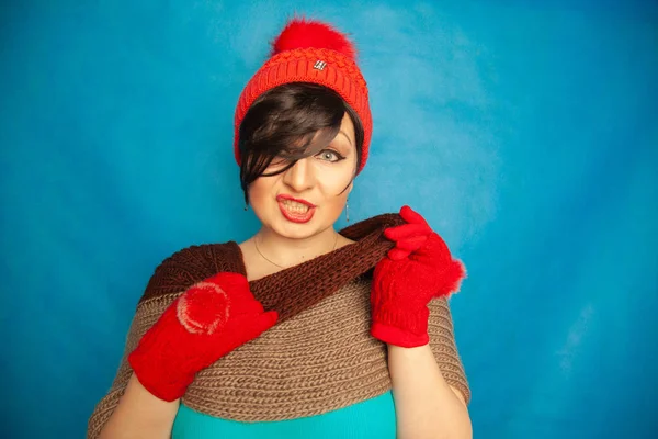 漂亮的黑发女孩穿着时尚红色针织冬高和温暖美丽的手套在蓝色工作室坚实的背景 — 图库照片