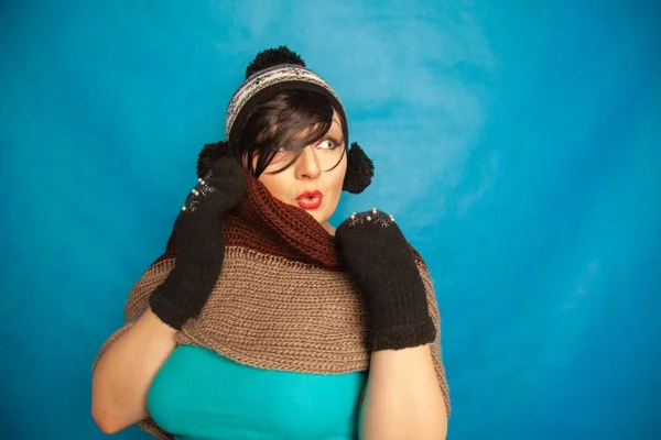 pretty brunette girl wearing fashion black knitted winter hat and warm beautiful mittens on blue studio solid background
