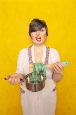 şirin duygusal esmer açlıktan, ağırlık kaybı için bir diyet takip etmeye çalışıyorum. boş bir pot ve bir santimetre kaset elinde pembe bir elbise içinde bir kadın durumda.