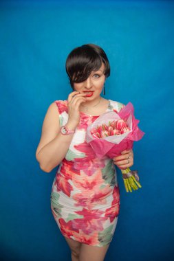 Bahar elbise sevimli gülümseyen kız stüdyoda mavi bir arka plan üzerinde tulip buket pembe taze tutar. o gerçekten hediye ve kesinlikle mutlu bulunuyor.