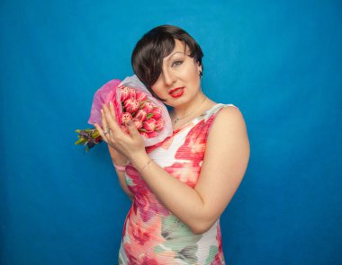 Bahar elbise sevimli gülümseyen kız stüdyoda mavi bir arka plan üzerinde tulip buket pembe taze tutar. o gerçekten hediye ve kesinlikle mutlu bulunuyor.