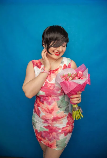 드레스에 귀여운 스튜디오에서 파란색 배경에 분홍색 신선한 꽃다발을 하고있다 그녀는 — 스톡 사진