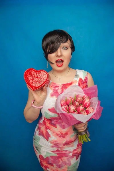 Bahar elbise sevimli gülümseyen kız stüdyoda mavi bir arka plan üzerinde tulip buket pembe taze tutar. o gerçekten hediye ve kesinlikle mutlu bulunuyor.